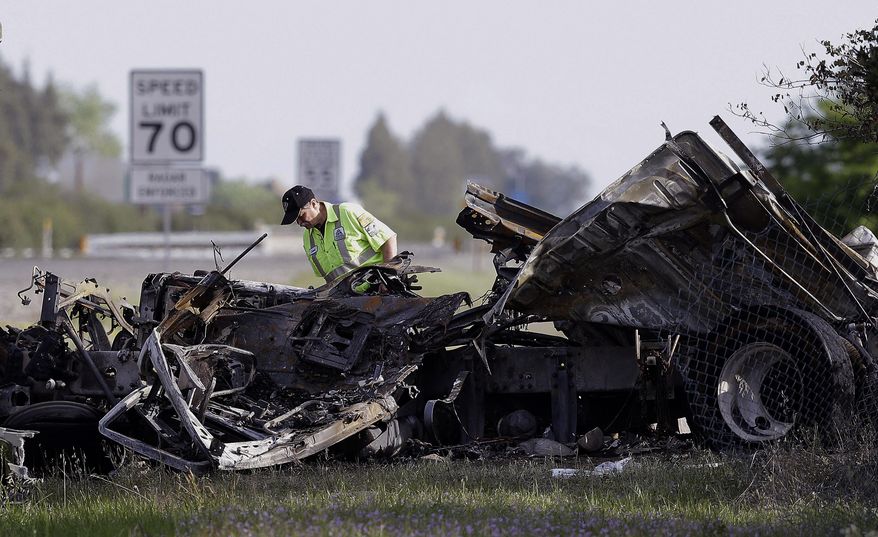 A worker looks over the demolished cab of FedEx truck that crashed into a tour bus on Interstate 5 Thursday in Orland, Calif., Friday, April 11, 2014. At least ten people were killed and dozens injured in the fiery crash between the truck and a bus carrying high school students on a visit to a Northern California College. (AP Photo/Jeff Chiu)