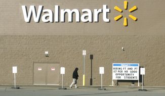 A shopper walks next to a Walmart store on Friday, Feb. 28, 2014, in Williston, N.D., near a sign advertising a $17 hourly wage for new employees — a rate higher than in many cities. (AP Photo/Martha Irvine) ** FILE ** 