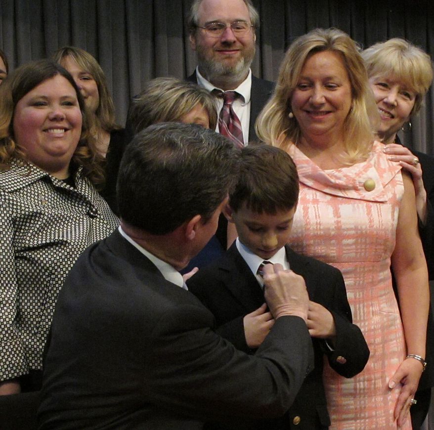 Kansas Gov. Sam Brownback adjusts 8-year-old Brad Eckart's tie before taking a group photo with parents of children with autism who supported a new law requiring limited health insurance coverage for treatment, Wednesday, April 16, 2014, in Overland Park. Brad's mother, to his right, Heidi Eckart, estimates the family has spent $500,000 on treating him. (AP Photo/John Hanna)