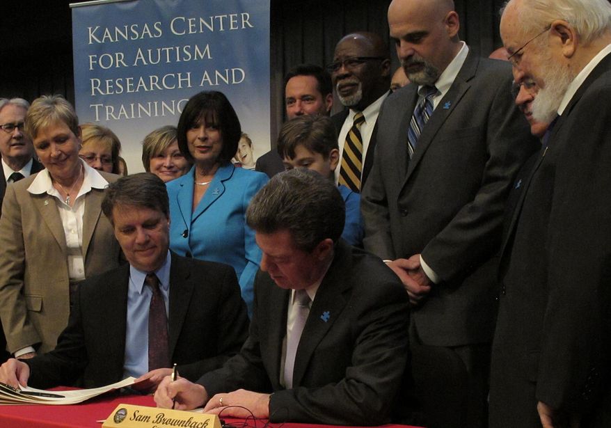 Kansas Gov. Sam Brownback signs legislation that will require health insurance companies to provide coverage for some services for children with autism, as legislators, parents and advocates for children with autism watch, Wednesday, April 16, 2014, in Overland Park, Kan. Lt. Gov. Jeff Colyer, a reconstructive plastic surgeon, is to the governor's immediate left. (AP Photo/John Hanna)