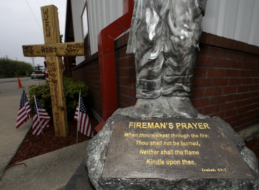 A statute with the prayer for fire fighters sits in front of a cross outside the volunteer fire department, Thursday, April 17, 2014, in West, Texas, that bears the names of some of those killed one year ago today when a fertilizer plant exploded. (AP Photo/Tony Gutierrez)