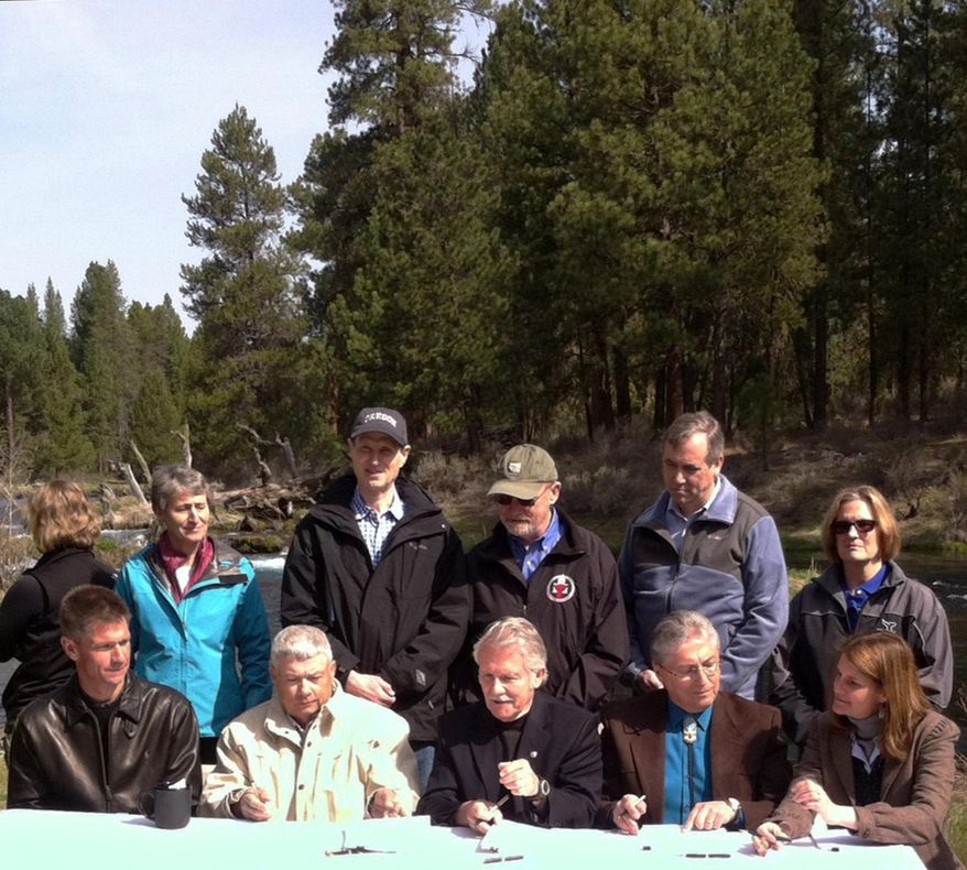 In ceremonies outside Chiloquin, Ore. on Friday, April 18, 2014, Gov. John Kitzhaber, center foreground, prepares to sign an agreement between Upper Klamath Basin cattle ranchers and the Klamath Tribes to share access to rivers and cooperate on restoring fish sacred to the tribes. He is flanked by representatives of the ranchers and the tribes. Behind them are Senators Ron Wyden, third from left background, and Jeff Merkley, second from right, and representatives of the Obama administration. (AP Photo/U.S. Fish and Wildlife Service, Matt Baun)