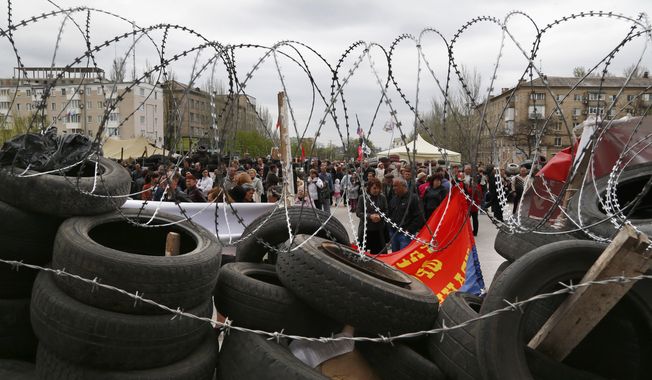 People stand at a barricade at the regional administration building that they had seized earlier in Donetsk, Ukraine, Sunday, April 20, 2014. The Ukrainian and Russian governments are reporting a shootout at a checkpoint set up by pro-Russian insurgents in eastern Ukraine that has left one person dead and others hospitalized with gunshot wounds. (AP Photo/Sergei Grits)