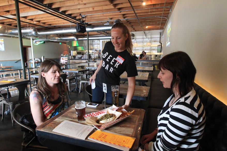 In this April 21, 2014 photo, Bar back Lori Campbell, center, serves food to Andrea Latimer, right, and Nichole Peterson at Beer Bar in Salt Lake City. Actor Ty Burrell, who plays bumbling dad Phil Dunphy on ABC's “Modern Family,” just opened Beer Bar, a beer garden-like eatery that serves 150 beers paired up with an array of house-made bratwursts, local breads and Belgian fries. The restaurant sports long tables and benches with high ceilings to evoke that Bavarian beer hall feel. (AP Photo/Rick Bowmer)