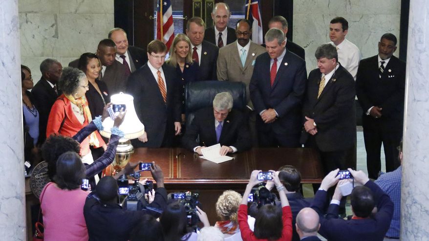 Surrounded by elected officials, Republican Gov. Phil Bryant, seated at center, signs the Teacher Pay Raise bill in the rotunda of the Capitol in Jackson, Miss. on Monday, April 22, 2014. The legislation gives public school teachers two across-the-board pay raises worth $2,500 over the next two years, and would eligible for merit payments in 2016-2017. (AP Photo/Rogelio V. Solis)