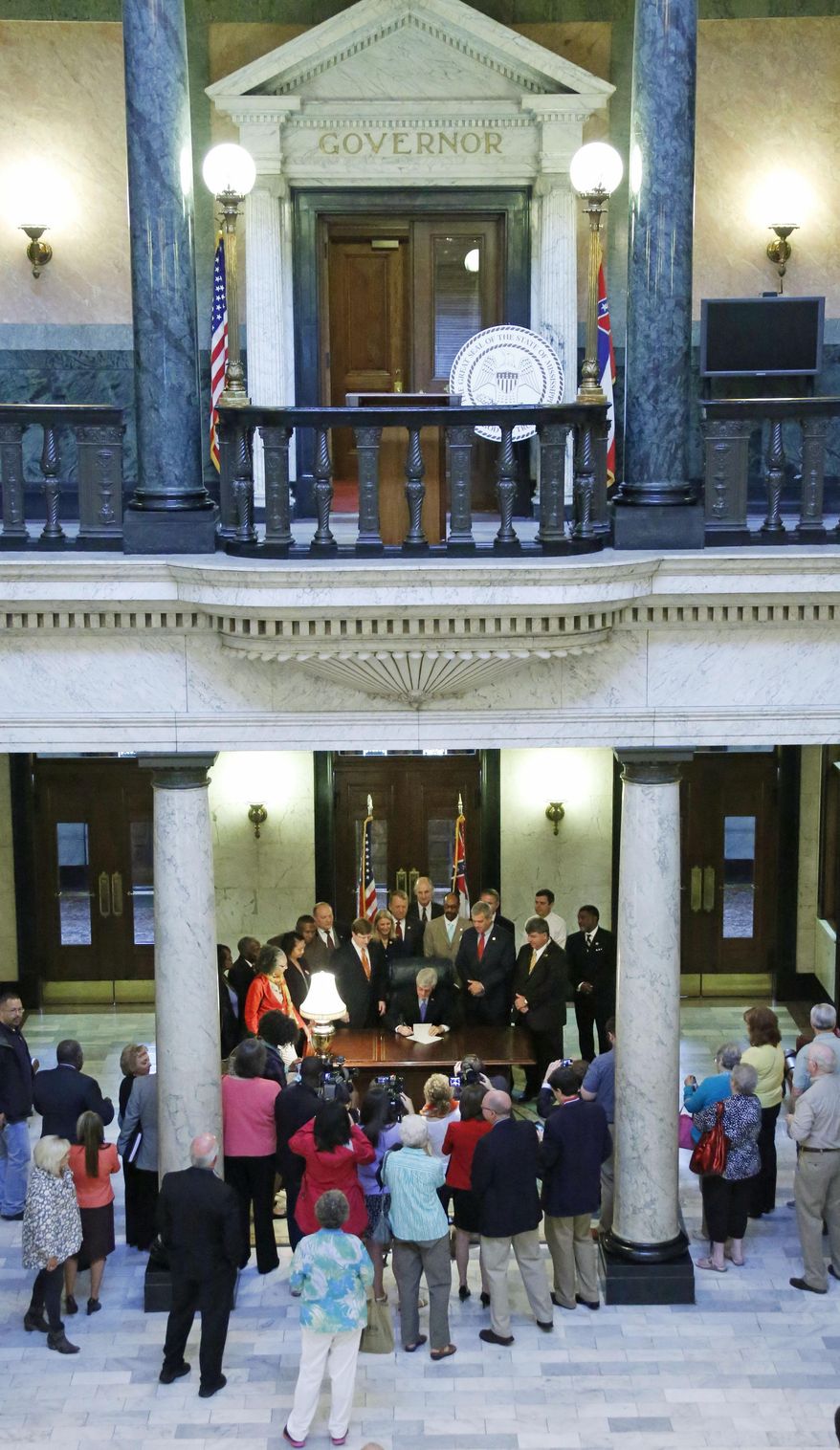 Surrounded by elected officials, Republican Gov. Phil Bryant, seated at center, signs the Teacher Pay Raise bill in the rotunda of the Capitol in Jackson, Miss., Monday, April 22, 2014. The legislation gives public school teachers two across-the-board pay raises worth $2,500 over the next two years, and eligibility for merit payments in 2016-2017. (AP Photo/Rogelio V. Solis)