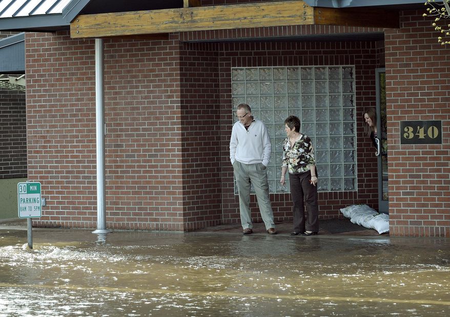 In this photo taken on Tuesday, April 22, 2014, from left, Trevor Griesmeyer, Sharon Waters and Deanna Grove watch the flooding in front of Barker Uerlings Insurance that was caused by a broken water main in Corvallis, Ore. The city estimated Wednesday that 800,000 gallons of water eventually poured out of the 20-inch iron pipe. (AP Photo/The Corvallis Gazette-Times, Andy Cripe)