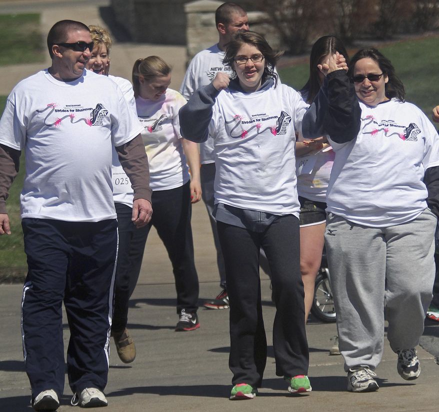 In this April 5, 2014 photo, former Quincy University student Shannon Peters, center, pumps her fist she heads out on a one-mile walk around the school's campus with her mother and father, Matt, left, and Mary Peters. The walk was part of the "Strides for Shannon" fundraiser. Shannon Peters was seriously injured when struck by a car on Jan. 7, 2013. (AP Photo/The Quincy Herald-Whig, Phil Carlson)