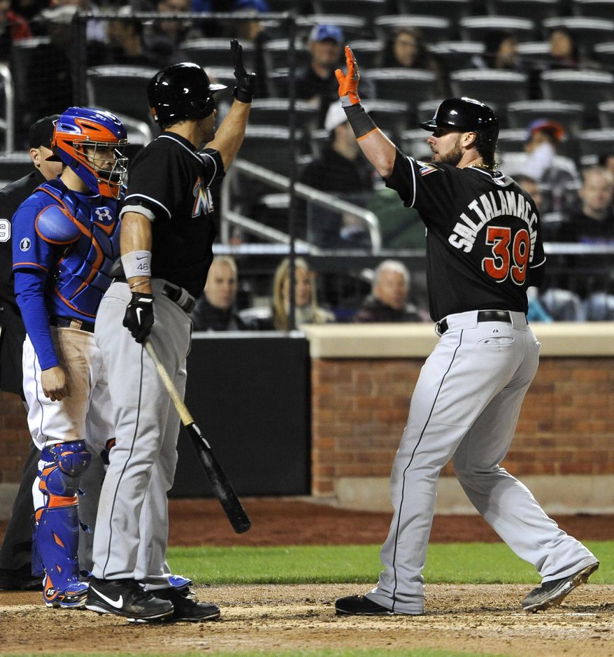 New York Mets catcher Travis d'Arnaud, left, watches Miami Marlins' Garrett Jones greet Jarrod Saltalamacchia (39) after Saltalamacchia hit a solo home run off Mets relief pitcher Gonzalez Germen in the eighth inning of a baseball game at Citi Field on Friday, April 25, 2014, in New York. Jones followed with a solo home run. (AP Photo/Kathy Kmonicek)
