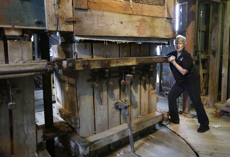 In this Wednesday, April 23, 2014 photo, Linda Russell, director of the Burton Cotton Gin Museum, demonstrates how the cotton presses can be rotated in Burton, Texas. The device compresses ginned cotton into 500-pound bales. The Burton Farmers Gin is the oldest working gin in the country at 100 years old.(AP Photo/Pat Sullivan)