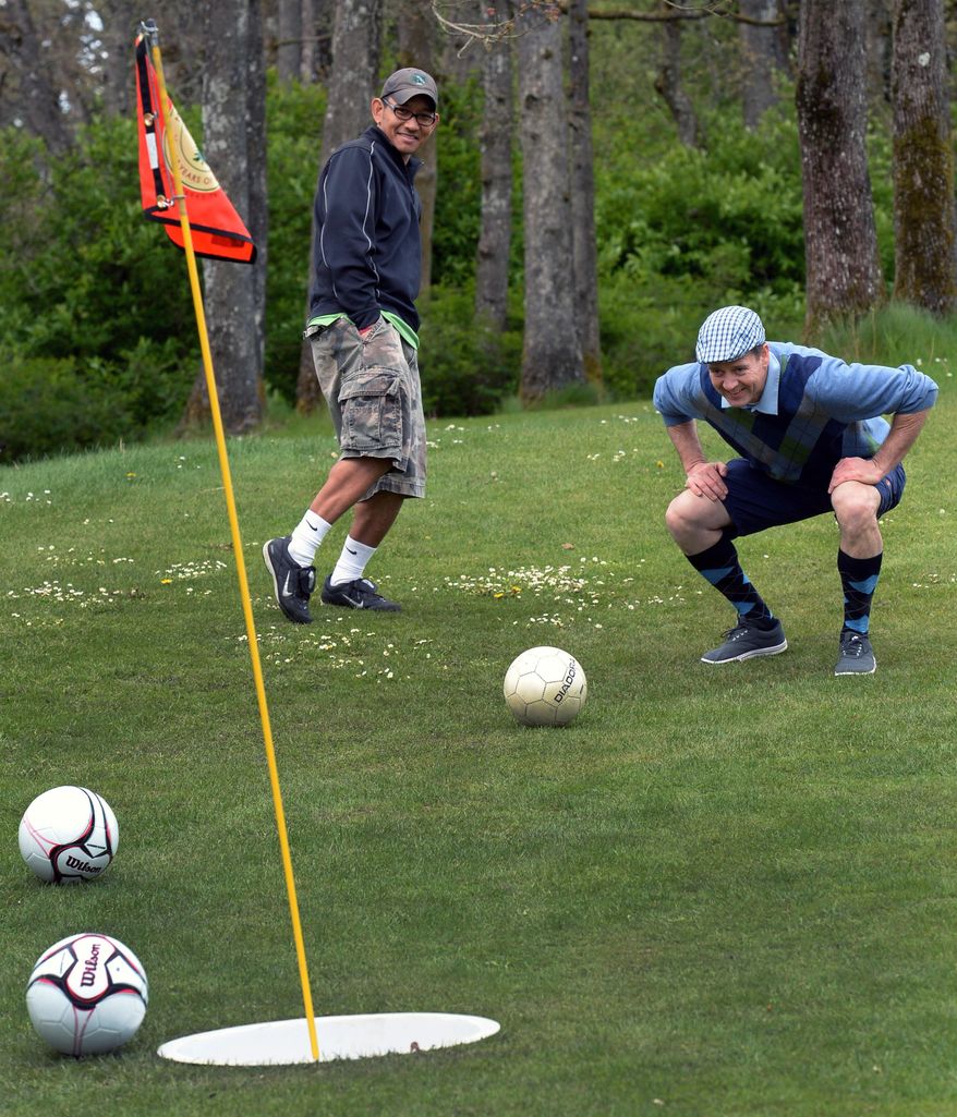 In this April 26, 2014 photo, Meadow Park Golf Course superintendent Chris Goodman, right, watches his shot miss to the amusement of Dennis Roque during a round of Footgolf at Meadow Park Golf Course, in Tocoma, Wash. In addition to the 21-inch-wide holes, there are a few other changes to the golf game. The holes are shorter and one can play 18 holes in about 90 minutes. (AP Photo/The News Tribune, Drew Perine)