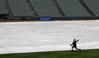 A member of the Baltimore Orioles warms up alongside a tarp covering the infield as rain falls before a scheduled baseball game between the Orioles and the Pittsburgh Pirates, Tuesday, April 29, 2014, in Baltimore. Officials postponed the game due to the rain, and it has been rescheduled for Thursday. (AP Photo/Patrick Semansky)