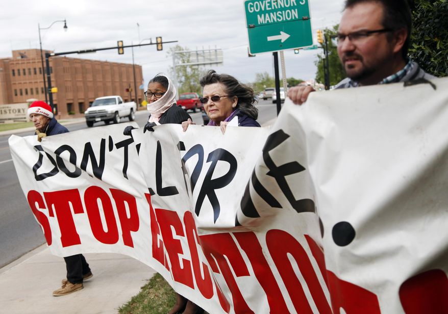 John Walters, Jana Lewis-Harkins, Fannie Bates and Aaron Baker, from left, hold a banner during a protest at the Governor's Mansion in Oklahoma City on Tuesday, April 29, 2014, over the planned execution of two inmates. An execution that used a new drug combination left an Oklahoma inmate writhing and clenching his teeth on the gurney later Tuesday, leading prison officials to halt the proceedings before the inmate's eventual death from a heart attack. (AP Photo/The Oklahoman, KT King)
