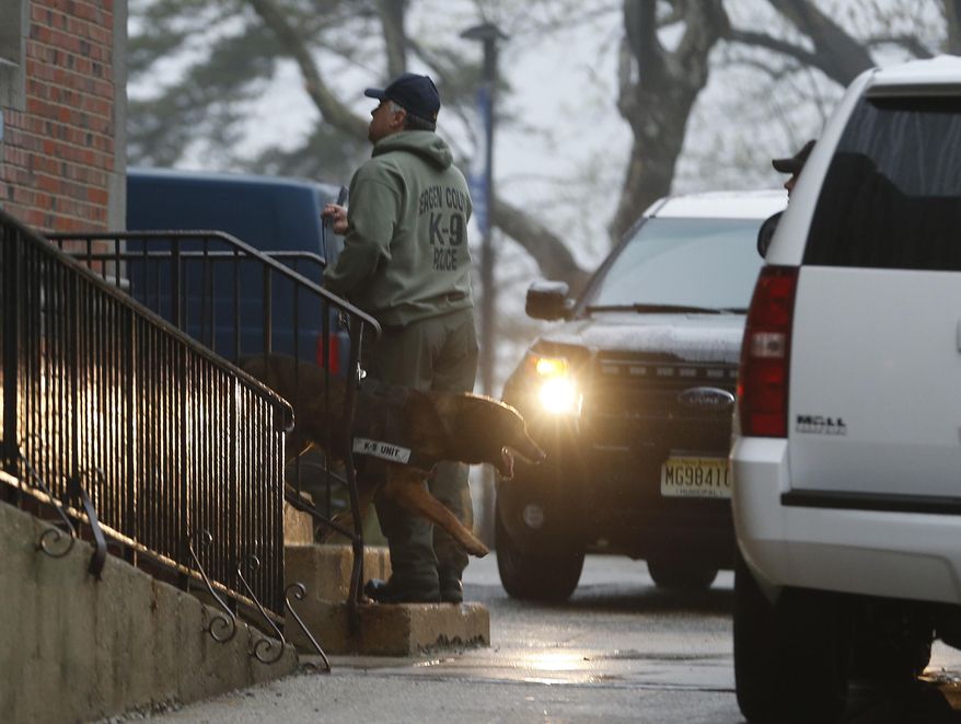 A Bergen County Police officer walks with a police dog outside of Teaneck High School, where at least 60 students were arrested during an overnight break-in, Thursday, May 1, 2014, in Teaneck, N.J. Officers responded to a burglar alarm at the school around 2:30 a.m. Thursday, found urine in the hallways, petroleum jelly on doorknobs, desks flipped over and balloons throughout the building. (AP Photo/Julio Cortez)