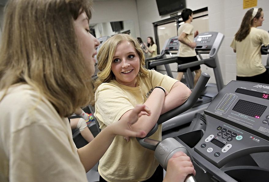 ADVANCE FOR USE SUNDAY, MAY 4 AND THEREAFTER - In this April 11, 2014 photo, adaptive physical education leader Katelyn Lowery, 18, right, encourages Elizabeth Limanowski, 16, as Limanowski works out on a stationary bike at Lincoln-Way North High School in Frankfort, Ill. Lowery, a senior, is one of the eight local 2014 Golden Apple Scholars, a program that fosters young educators and provides tuition assistance for college. (AP Photo/The Herald-News, Rob Winner) MANDATORY CREDIT