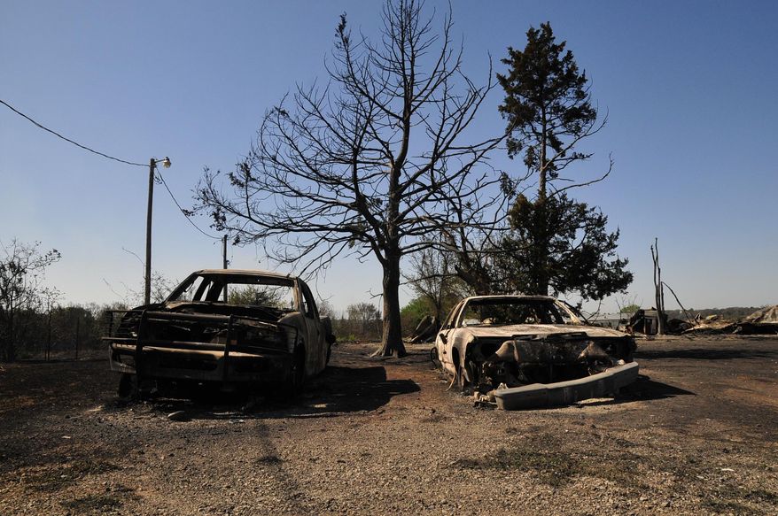 The charred remains of two cars are left on Monday, May 5, 2014, in Guthrie, Okla., the day after a wildfire tore through the area. Firefighters worked through the night and into early Monday to battle the large wildfire that destroyed at least six homes and left at least one person dead after a controlled burn spread out of control in central Oklahoma. (AP Photo/Nick Oxford)
