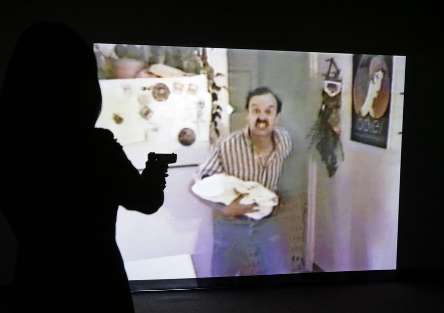 In this Feb. 27, 2014 photo, a television reporter uses a specially modified gun to try to shoot a hostage taker during a demonstration of the Harris County district attorney's shooting simulator, in Houston. The interactive way of illustrating the legal concept of deadly force is part of the unique training that Houston-area grand jurors can receive before they begin hearing cases. But critics argue that it puts grand jurors in a pro-law enforcement mindset. One Houston defense attorney recently unsuccessfully challenged the simulator’s use, calling it mind manipulation. (AP Photo/Pat Sullivan)