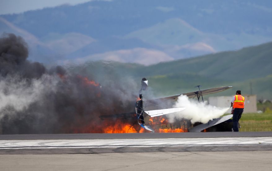 A worker fights a fire after a vintage biplane crashed upside-down on a runway at an air show at Travis Air Force Base in Fairfield, Calif., Sunday, May 4, 2014. The pilot, Edward Andreini, 77, of Half Moon Bay, was killed when the plane, flying low over the tarmac, crashed and caught fire. (AP Photo/Bryan Stokes)