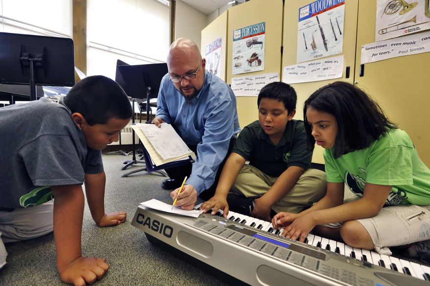 In this April 22, 2014 photo, Conrad Kehn, lead artist facilitator for the Very Young Composers program, helps students compose during music class, at Cole Elementary, in Denver. After years of promoting hefty education reforms, Colorado lawmakers this term focused on a school overhaul that was both more popular and more problematic, giving schools money to make the reforms and backfill years of recession-era cuts. (AP Photo/Brennan Linsley)