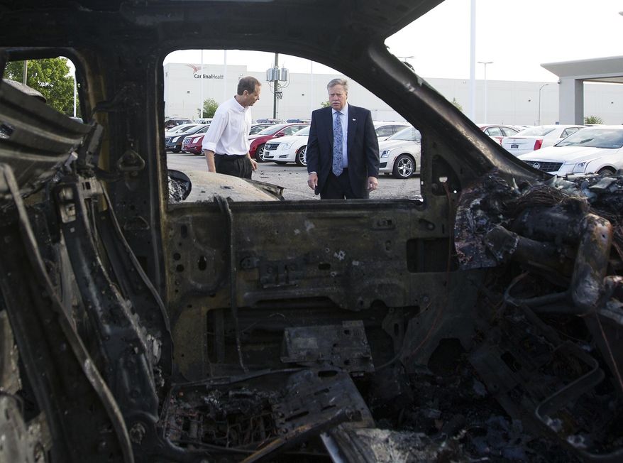 Shop Foreman Sid Huhn, left, and General Manager Steven Hainline, right, walk near a row of burnt Cadillac Escalades at Tom Peacock Cadillac Tuesday, May 6, 2014, in Houston. The vehicles burned to the ground after a wreck sparked a fire igniting the Escalades on the lot. General Manager Steven Hainline said the damage totals nearly $750,000. (AP Photo/Houston Chronicle, Cody Duty)