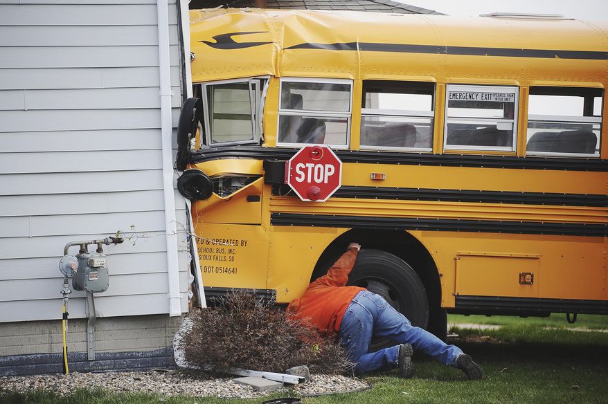 Crews with Sioux Falls Fire and Rescue and a tow truck driver from Ace Towing work to remove a bus from a house after it crashed into the house and a house across the street on Tuesday, May 6, 2014, in Sioux Falls, S.D. There were no children were on the bus at the time of the crash, and the bus driver, 66, was taken to the hospital with a head injury. (AP Photo/Argus Leader, Joe Ahlquist) NO SALES
