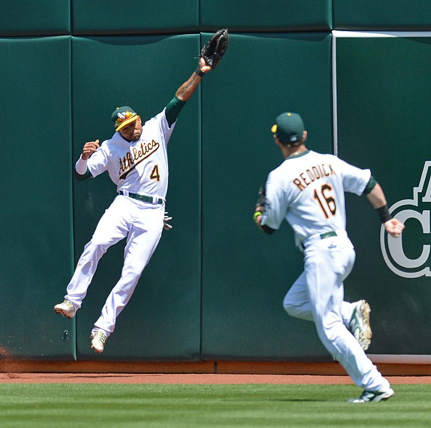 Oakland Athletics' Coco Crisp, left, leaps to make the catch on a ball hit by Seattle Mariners' Kyle Seager in the third inning of a baseball game Wednesday, May 7, 2014, in Oakland, Calif. Crisp hit the wall on the play, and left the game. At right is A's Josh Reddick (16). (AP Photo/The Contra Costa Times, Don Rosenstrauch)
