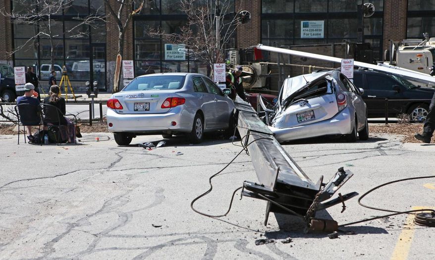 A crane lies on its side on Milwaukee's east side on Friday, May 9, 2014. Two people, left, who were with their dog inside one of the cars were injured because of the fall but didn't seek medical attention, according to police. Three other damaged vehicles were unoccupied. (AP Photo/Milwaukee Journal Sentinel, Michael Sears)