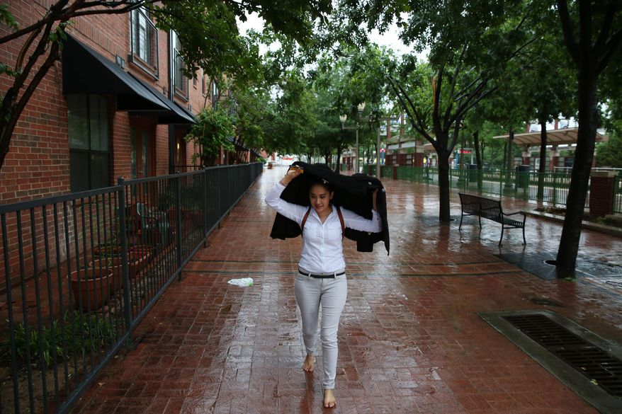 Jennifer Reyes, of Plano, covers herself while walking barefoot on her way home from work amid thunderstorms over downtown Plano, Texas on May 8, 2014. Thunderstorms are moving across the Plains, bringing strong winds and tornadoes and prompting a high-water rescue of five children.(AP Photo/The Dallas Morning News, Andy Jacobsohn) MANDATORY CREDIT, NO SALES, MAGS OUT, TV OUT, INTERNET USE BY AP MEMBERS ONLY