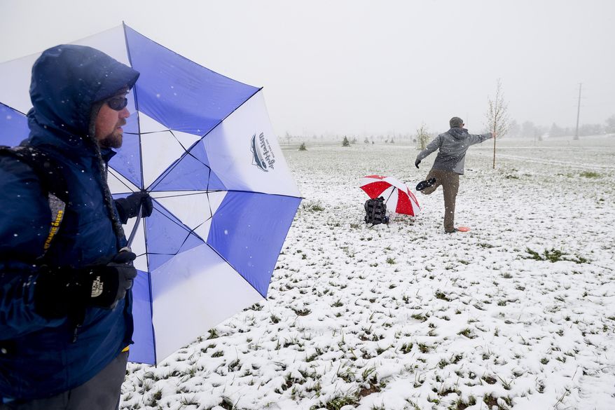 Mitch Sonderfan shields himself from the snow and wind with an umbrella as Pat Blazek throws a disc golf while competing in a tournament Sunday, May 11, 2014, at Aggie Greens in Fort Collins, Colorado. Snow is expected to fall through Monday, with highs reaching the sixties later this week. (AP Photo/The Coloradoan, Erin Hull)