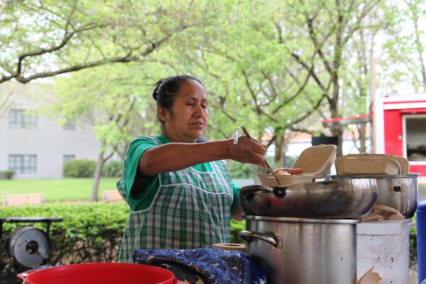 In this Tuesday, April 15, 2014 photo, Paula Asuncion scoops traditional Oaxacan mole sauce onto a dish of tamales at the Lloyd Farmers Market in Portland, Oregon. Asuncion once worked in the fields, but after participating in a micro-business development program she now sells tamales at several farmers markets and runs a catering service. (AP Photo/Gosia Wozniacka)