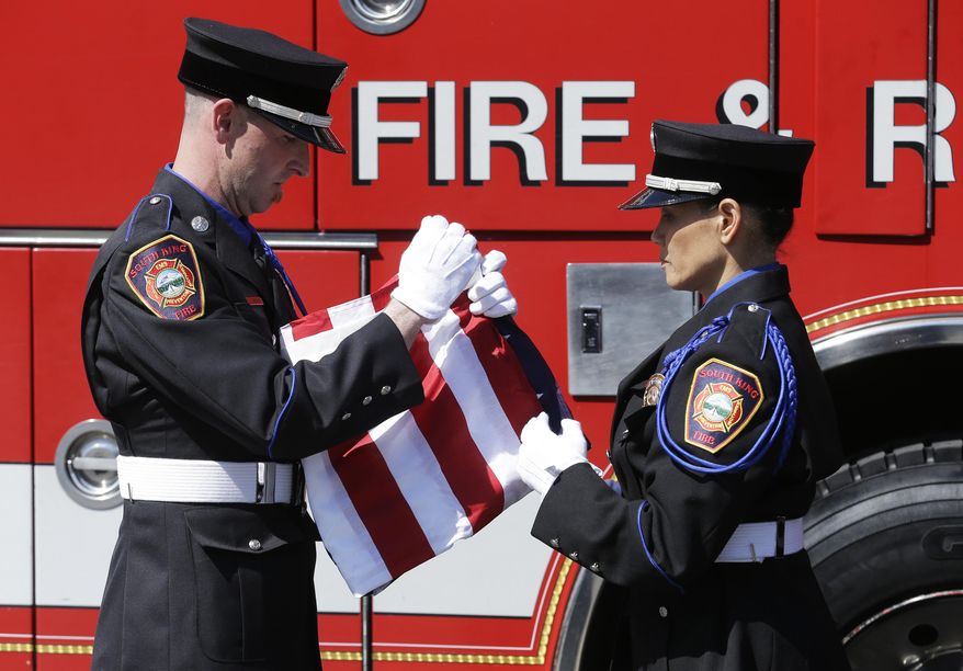 South King Co. Fire and Rescue lt. Chris Andersen, left, and firefighter Wendy Chinn, right, fold a U.S. flag Monday, May 12, 2014, that was draped over a piece of limestone that was part of the building at the Pentagon in Washington, DC, before it was destroyed in the September 11, 2001 terrorist attacks. The stone was delivered Monday during a ceremony at the Alaska Airlines cargo facility in Seatac, Wash., and will be part of a Sept. 11th memorial in Federal Way, Wash. that will be dedicated on Sept. 11, 2014, and also contains a beam from the World Trade Center in New York and a rock from the field in Shanksville, Pa., where United flight 93 crashed during the attacks. (AP Photo)