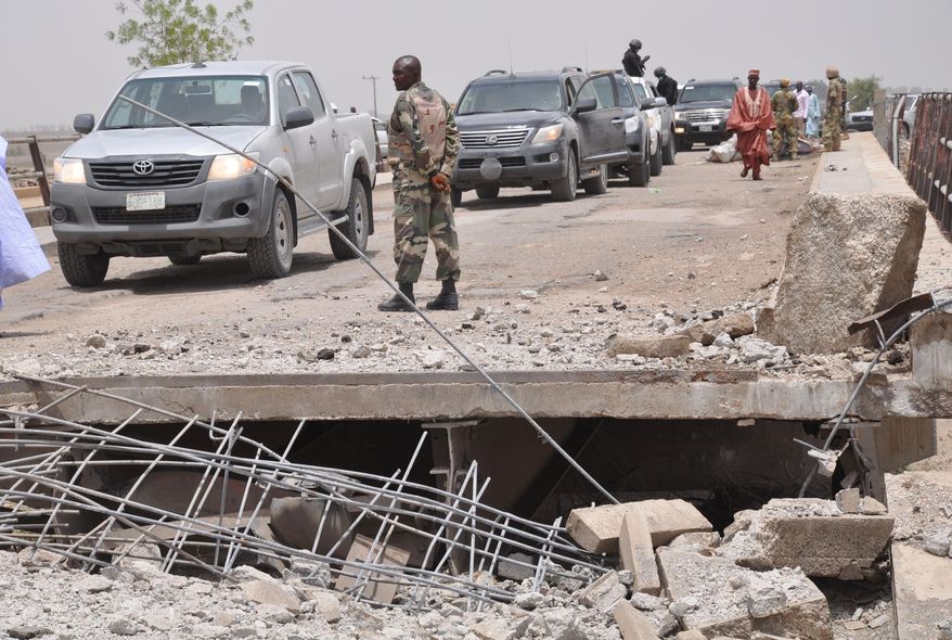 In this photo taken Sunday May 11, 2014. A soldier and other government officials inspect the bridge that was bombed following an attack by Islamic militants last week in Gambaru, Nigeria. Many brutalized residents of the once bustling town of Gamboru say they are moving across the border to Cameroon because they cannot trust the Nigerian government to protect them, after repeated attacks by Islamic militants, including an attack a few days ago that killed some hundreds of people with more than 1,000 shops, dozens of homes and 314 trucks and cars bombed and burned out. (AP Photo/Jossy Ola)