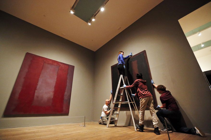Tate Modern employees pose for the photographers in front of Mark Rothko’s  'Black on Maroon' mural, right, and 'Red on Maroon section 4 1959' mural, left, in London, Tuesday, May 13, 2014. Tate Modern is putting 'Black on Maroon' back on display Tuesday, more than a year and a half after it was defaced with black ink by a vandal trying to draw attention to an obscure artistic movement. The gallery has spent 18 months working on the abstract painting, whose surface is made up of layers of oil, pigment, resin, egg and glue. Tate experts said the ink soaked in as far as the back of the canvas, requiring delicate work to remove it and restore the painting's layers. Wlodzimierz Umaniec received a two-year jail sentence for scrawling "a potential piece of yellowism" on the painting to draw attention to Yellowism, an artistic movement he co-founded.(AP Photo/Lefteris Pitarakis)