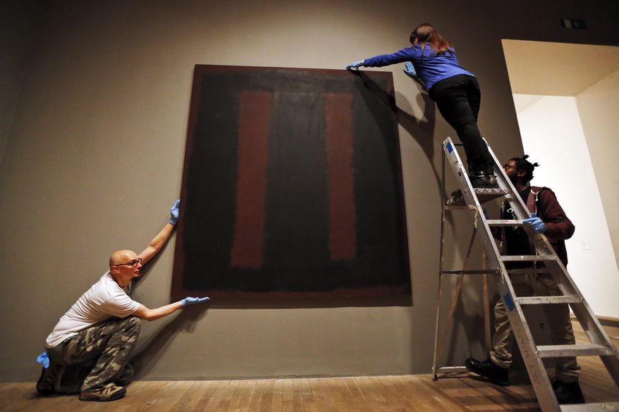 Tate Modern employees pose for the photographers in front of Mark Rothko’s mural 'Black on Maroon', in London, Tuesday, May 13, 2014. Tate Modern is putting the mural back on display Tuesday, more than a year and a half after it was defaced with black ink by a vandal trying to draw attention to an obscure artistic movement. The gallery has spent 18 months working on the abstract painting, whose surface is made up of layers of oil, pigment, resin, egg and glue. Tate experts said the ink soaked in as far as the back of the canvas, requiring delicate work to remove it and restore the painting's layers. Wlodzimierz Umaniec received a two-year jail sentence for scrawling "a potential piece of yellowism" on the painting to draw attention to Yellowism, an artistic movement he co-founded.(AP Photo/Lefteris Pitarakis)