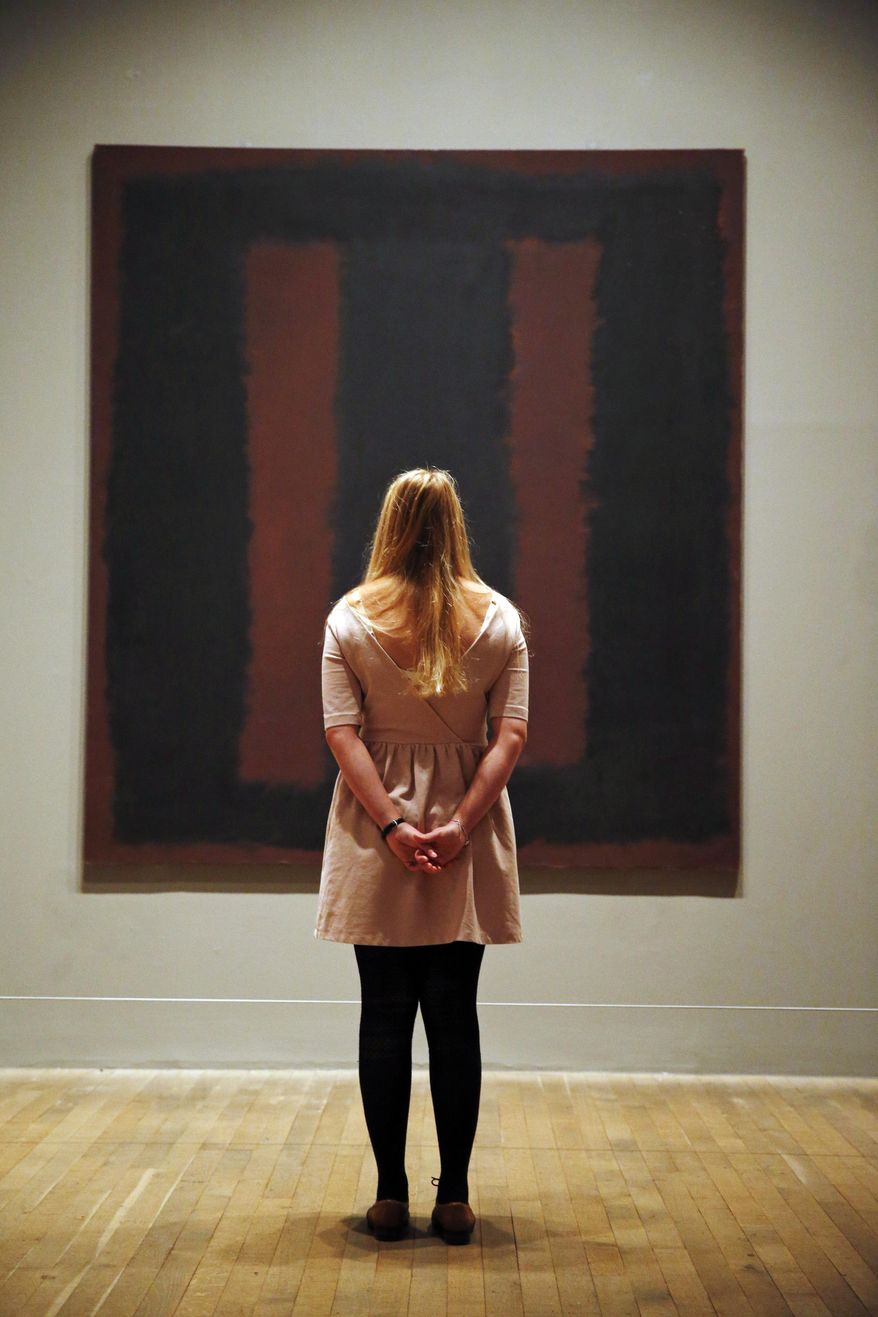 A Tate Modern employee poses for the photographers in front of Mark Rothko’s mural 'Black on Maroon', in London, Tuesday, May 13, 2014. Tate Modern is putting the mural back on display Tuesday, more than a year and a half after it was defaced with black ink by a vandal trying to draw attention to an obscure artistic movement. The gallery has spent 18 months working on the abstract painting, whose surface is made up of layers of oil, pigment, resin, egg and glue. Tate experts said the ink soaked in as far as the back of the canvas, requiring delicate work to remove it and restore the painting's layers. Wlodzimierz Umaniec received a two-year jail sentence for scrawling "a potential piece of yellowism" on the painting to draw attention to Yellowism, an artistic movement he co-founded.(AP Photo/Lefteris Pitarakis)