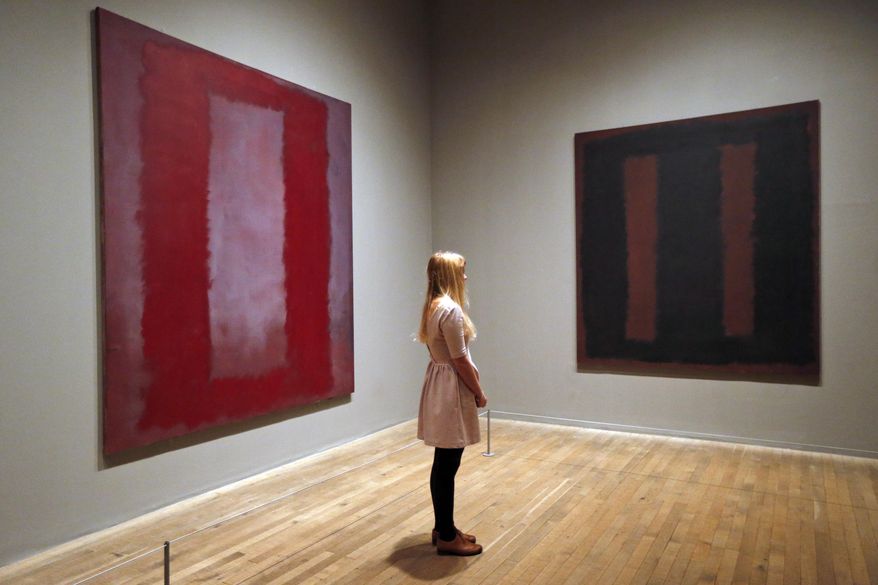 A Tate Modern employee poses for the photographers in front of Mark Rothko’s  'Black on Maroon' mural, right, and 'Red on Maroon section 4 1959' mural, left, in London, Tuesday, May 13, 2014. Tate Modern is putting 'Black on Maroon' back on display Tuesday, more than a year and a half after it was defaced with black ink by a vandal trying to draw attention to an obscure artistic movement. The gallery has spent 18 months working on the abstract painting, whose surface is made up of layers of oil, pigment, resin, egg and glue. Tate experts said the ink soaked in as far as the back of the canvas, requiring delicate work to remove it and restore the painting's layers. Wlodzimierz Umaniec received a two-year jail sentence for scrawling "a potential piece of yellowism" on the painting to draw attention to Yellowism, an artistic movement he co-founded.(AP Photo/Lefteris Pitarakis)