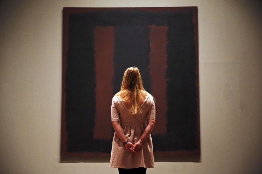 A Tate Modern employee poses for the photographers in front of Mark Rothko’s mural 'Black on Maroon', in London, Tuesday, May 13, 2014. Tate Modern is putting the mural back on display Tuesday, more than a year and a half after it was defaced with black ink by a vandal trying to draw attention to an obscure artistic movement. The gallery has spent 18 months working on the abstract painting, whose surface is made up of layers of oil, pigment, resin, egg and glue. Tate experts said the ink soaked in as far as the back of the canvas, requiring delicate work to remove it and restore the painting's layers. Wlodzimierz Umaniec received a two-year jail sentence for scrawling "a potential piece of yellowism" on the painting to draw attention to Yellowism, an artistic movement he co-founded.(AP Photo/Lefteris Pitarakis)
