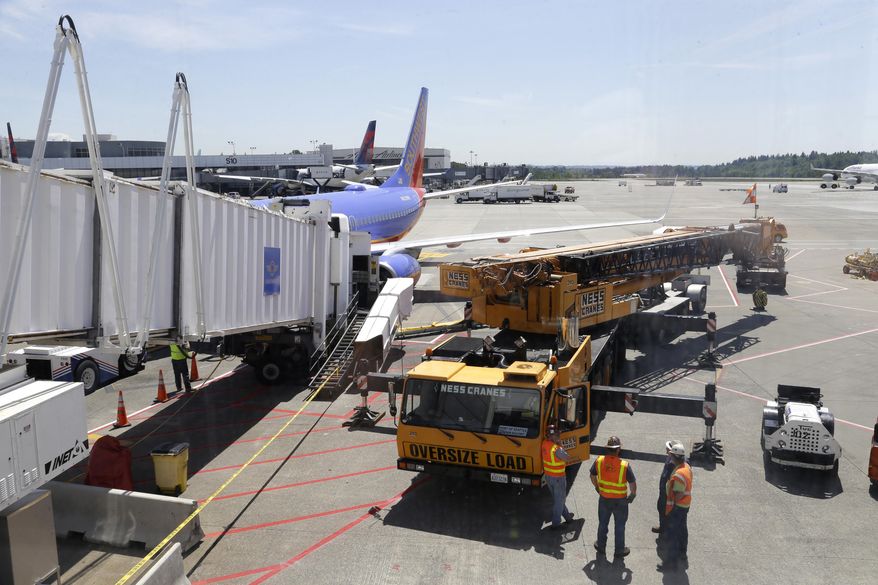 A large crane stands ready to lift a jetway, right, that had a mechanical failure and slowly lowered to the ground Tuesday, May 13, 2014, while connected to a Southwest Airlines airplane at Seattle-Tacoma International Airport. The incident happened as passengers from Phoenix were deplaning. The next leg of the flight to Chicago had to be canceled so the jetway could be removed from the airplane and a damage inspection could be completed. (AP Photo)