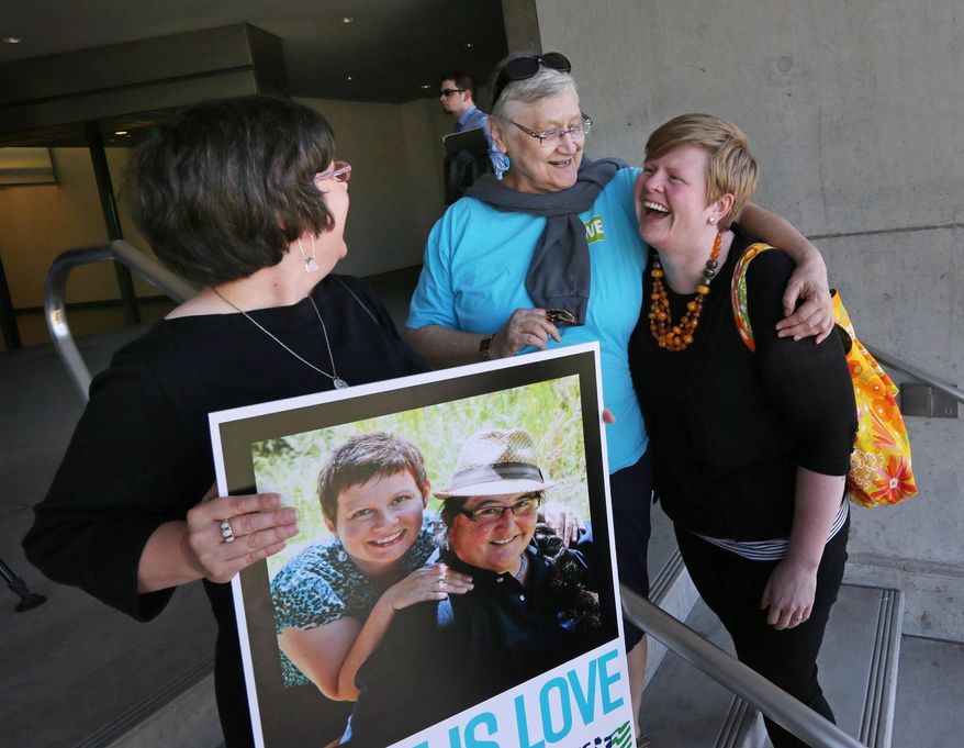 Victoria Smith Weiland, left, from Eugene, Ore., holds a picture of her and her partner Peggy McComb, as McComb hugs Aubrey Chonbold, right, on the steps of the Wayne L. Morse U.S. Courthouse Wednesday, May 14, 2014, in Eugene, Ore. A federal judge will hear arguments Wednesday about whether a national group can defend Oregon's ban on same-sex marriage because the state's attorney general has refused to do so. (AP Photo/The Register-Guard, Chris Pietsch)