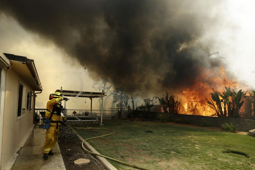 A Riverside firefighter moves away as shifting winds bring a plume of smoke overhead during a wildfire Thursday, May 15, 2014, in Escondido, Calif. One of the nine fires burning in San Diego County suddenly flared Thursday afternoon and burned close to homes, trigging thousands of new evacuation orders. (AP Photo/Gregory Bull)