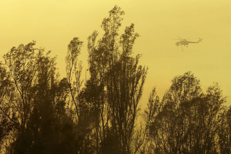 A helicopter transporting water flies over trees during a wildfire Thursday, May 15, 2014, in Escondido, Calif. One of the nine fires burning in San Diego County suddenly flared Thursday afternoon and burned close to homes, trigging thousands of new evacuation orders.(AP Photo/Gregory Bull)