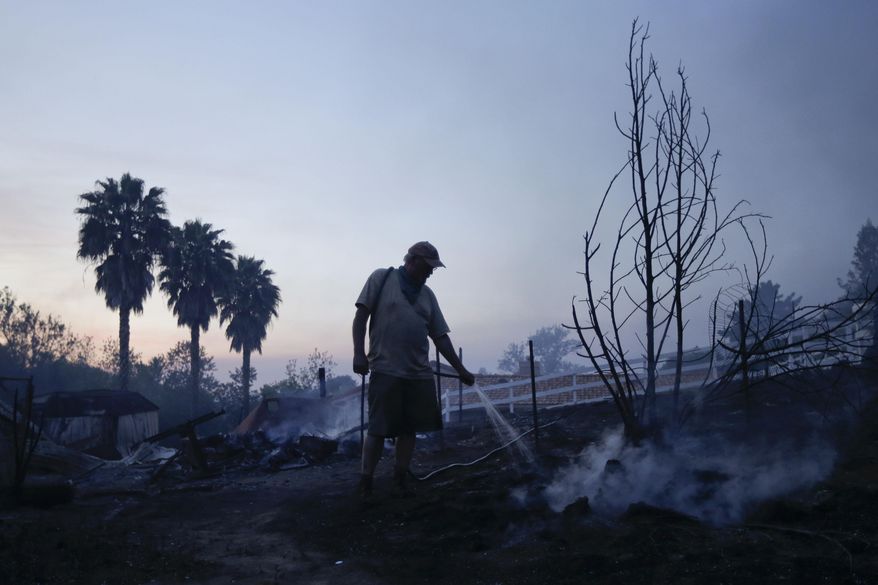Jeff Buchanan waters the scorched earth around a neighbor&#x27;s house that burned to the ground during a wildfire Thursday, May 15, 2014, in Escondido, Calif. One of the nine fires burning in San Diego County suddenly flared Thursday afternoon and burned close to homes, trigging thousands of new evacuation orders.(AP Photo/Gregory Bull)