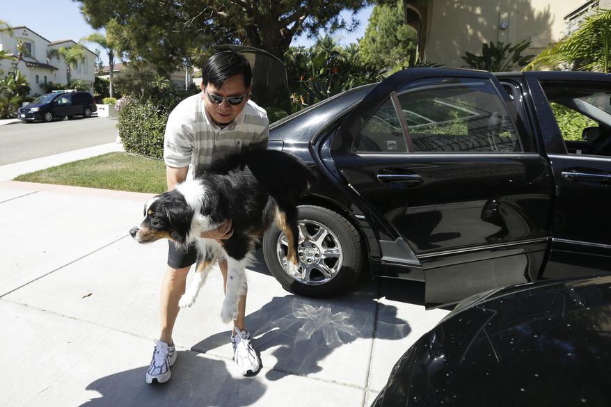 Midi Teng carries the family dog, Pup, out of the car as he arrives home from wildfire evacuations Friday, May 16, 2014, in Carlsbad, Calif. Some evacuation orders were lifted early Friday in an area near the fiercest of several wildfires in San Diego County, as crews building containment lines around the blazes hoped cooler temperatures will help them make further progress. (AP Photo/Gregory Bull)