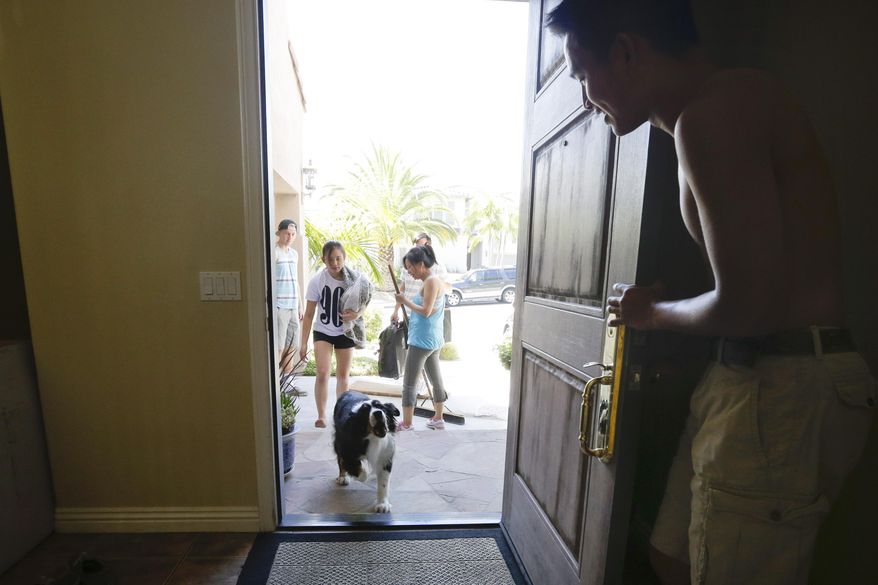 Sean Teng, right, holds open the front door as the Teng family dog Pup arrives home from wildfire evacuations, Friday, May 16, 2014, in Carlsbad, Calif. Behind, Snow, Teng sweeps while Annie and Logan Teng walk inside. Some evacuation orders were lifted early Friday in an area near the fiercest of several wildfires in San Diego County, as crews building containment lines around the blazes hoped cooler temperatures will help them make further progress. (AP Photo/Gregory Bull)