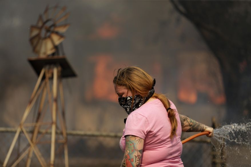 A woman douses water from a hose around her home as her neighbor&#x27;s home burns during a wildfire Thursday, May 15, 2014, in Escondido, Calif. One of the nine fires burning in San Diego County suddenly flared Thursday afternoon and burned close to homes, trigging thousands of new evacuation orders.(AP Photo/Gregory Bull)