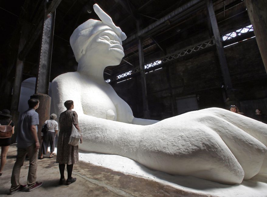 Visitors view “A Subtlety or the Marvelous Sugar Baby,” by artist Kara Walker, on display inside the former Domino Sugar Refinery, located in the Williamsburg neighborhood of Brooklyn, NY, Saturday, May 17, 2014. Four tons of sugar were used to create the 35-foot-high sphinx-like sculpture.The head of the large sculpture wears a kerchief and slightly exaggerated African features. Her breasts are exposed and her fists are thrust out, described by Walker as both submissive and domineering. (AP Photo/Richard Drew)