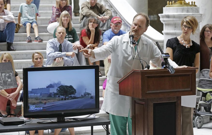 FILE - In this Sept. 11, 2013, file photo, Dr. Brian Moench stands next to a television, as it shows a heavy cloud of black smoke coming from Stericycle, a medical waste management company, during a medical waste incinerator protest at the Utah State Capitol, in Salt Lake City. A medical waste disposal company has identified a potential new home for a new incinerator in the Utah’s remote west desert. Doctors, families and others have pressed Stericycle, Inc. to close its North Salt Lake facility, saying it blankets the adjacent neighborhood with toxic smog. Company representatives say the facility is compliant with state regulations as it appeals a violation it received in 2013. (AP Photo/Rick Bowmer, File)