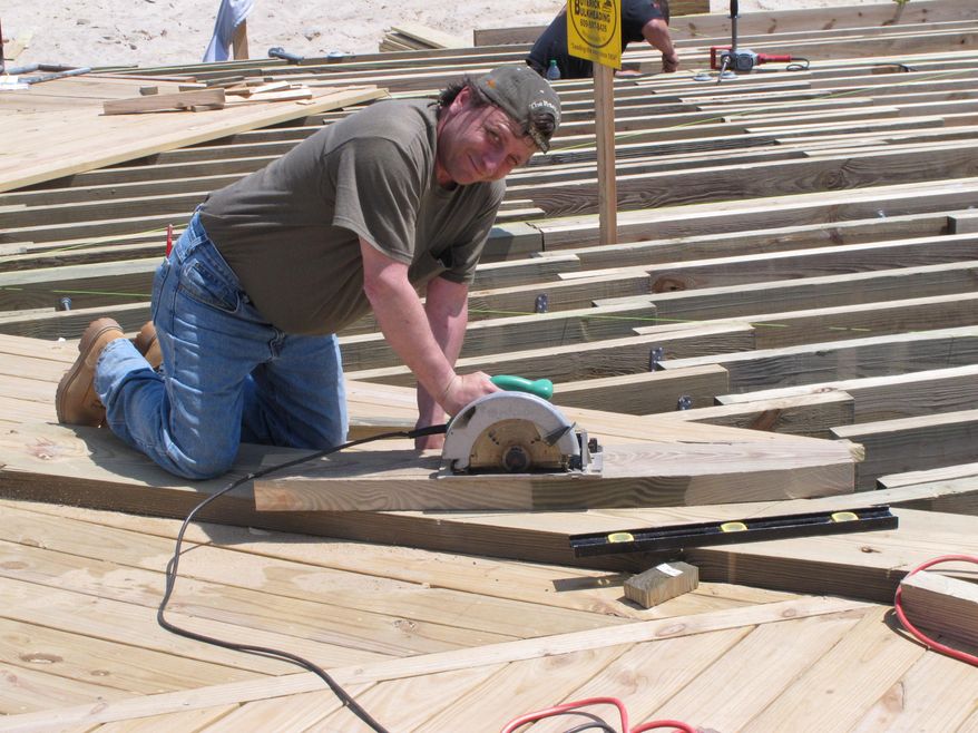 In this May 12, 2014 photo, a worker uses a saw to cut lumber on the Seaside Park N.J. boardwalk being rebuilt after a devastating fire last September. As the second summer after the Oct. 29, 2012 storm arrives, some at the Jersey shore are getting their lives back together, while for others, getting back to normal is still a long way off.(AP Photo/Wayne Parry)