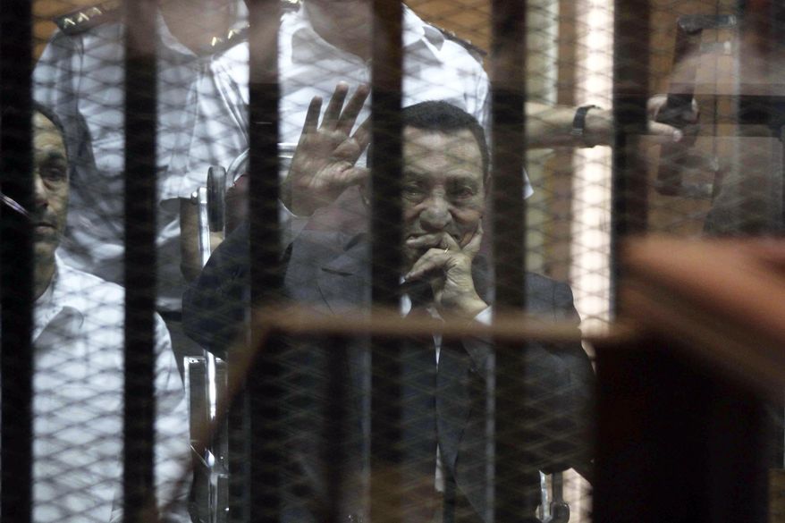 Ousted Egyptian President Hosni Mubarak, sitting in a defendants cage, waves during a court hearing as his son Gamal, left, in Cairo, Egypt, Wednesday, May 21, 2014. An Egyptian court has convicted Mubarak of embezzlement and sentenced him to three years in prison. Mubarak's two sons, one-time heir apparent Gamal and wealthy businessman Alaa, were also convicted Wednesday of graft and sentenced to four years in prison each in the same case. (AP Photo/ Hassan Mohammed)