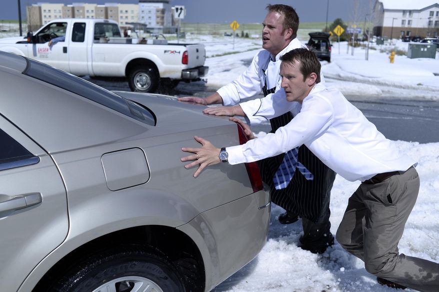 Chris Collins, left, and Paul Nellis, right, pushed a motorist out of the median on Tower Road Wednesday afternoon May 21, 2014. Hail piled more than a foot high on Tower Road stranded several vehicles following a storm that had both heavy rain and hail. Both men work at the Embassy Suites hotel near the airport. (AP Photo/The Denver Post, Karl Gehring)
